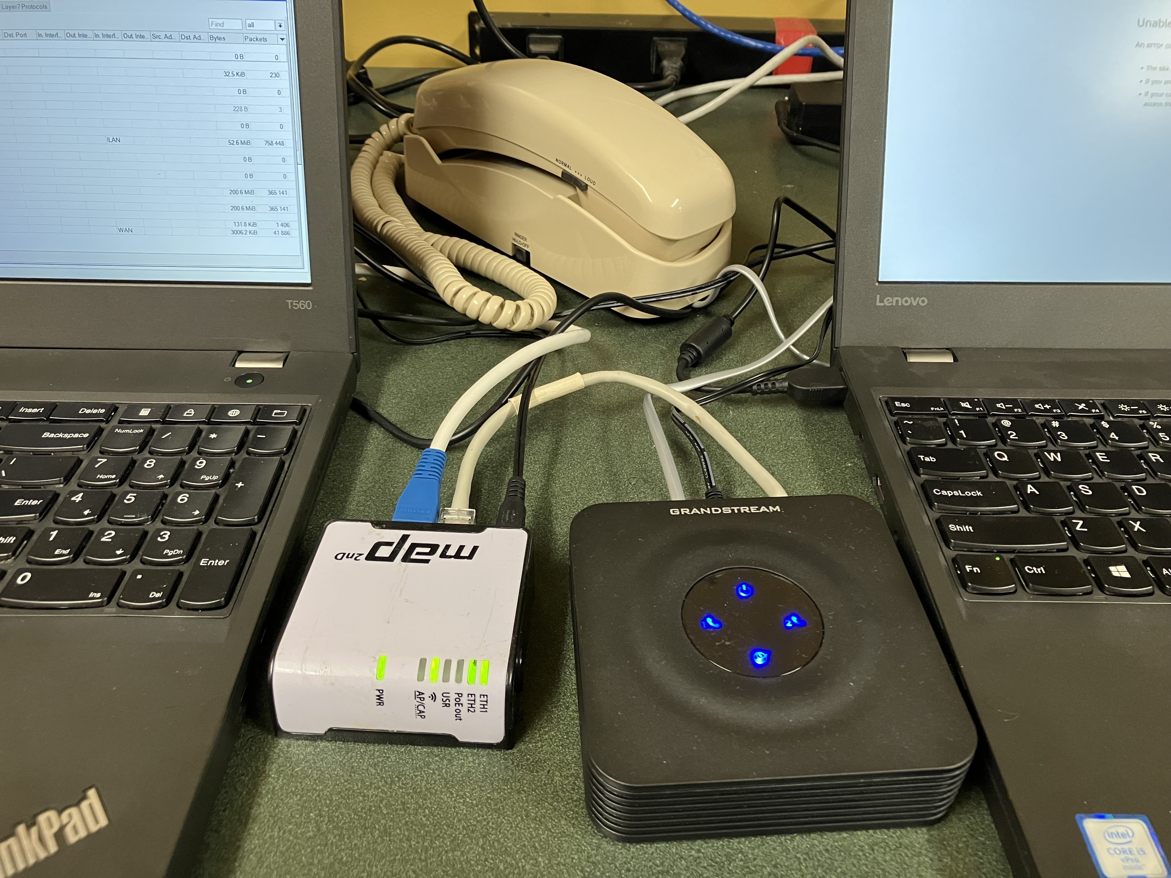 Image of an Analog Telephone Adapter, a Wi-Fi router device, a telephone handset, and two laptops for system configuration and testing.